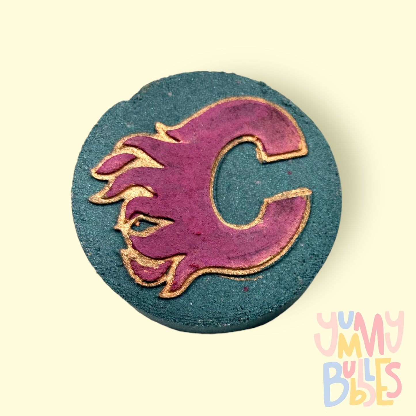 Hockey puck shaped bath bomb with a Calgary Flames logo in the center. Painted with red and gold and is a black bath bomb