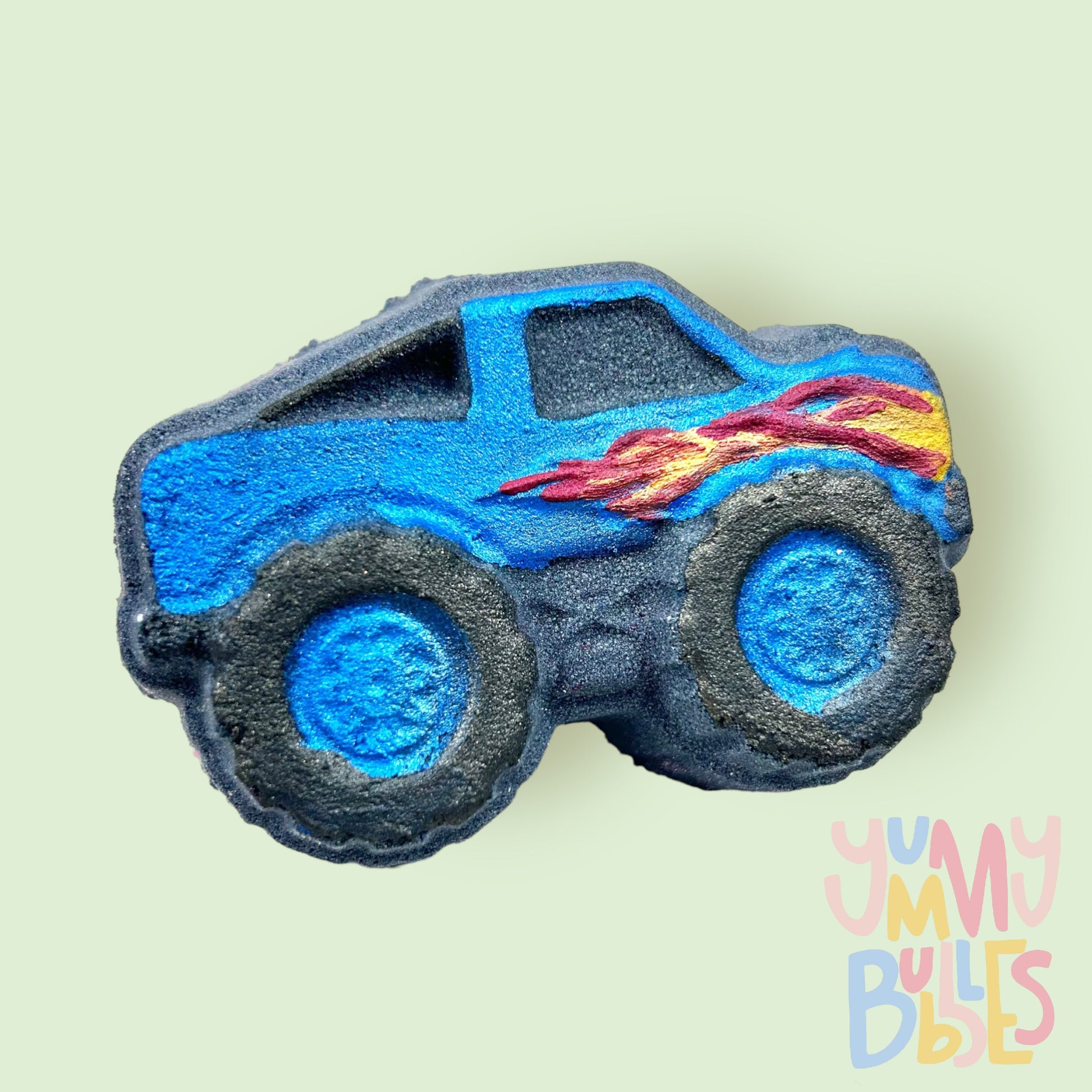 Monster truck shaped bath bomb with black base. Monster truck is painted with blue with a red and orange flame