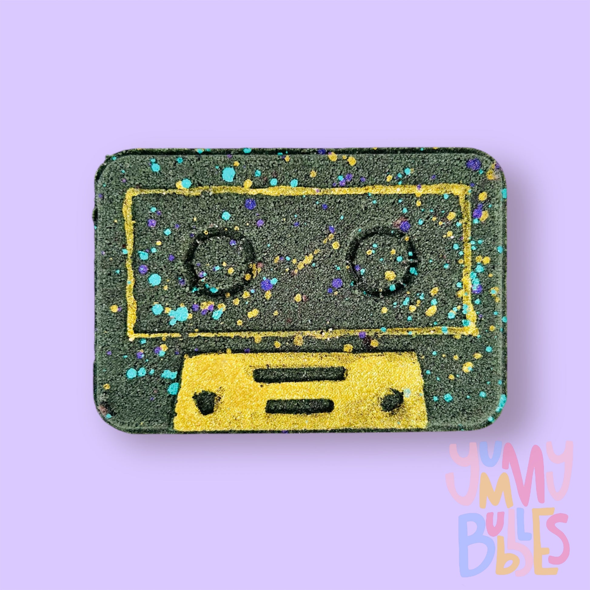Black Cassette shaped bath bomb with gold, blue, and purple paint.