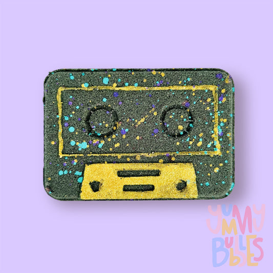 Black Cassette shaped bath bomb with gold, blue, and purple paint.