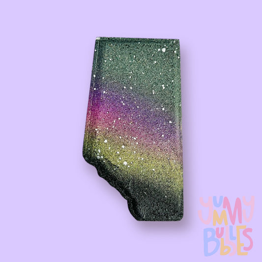 Black Alberta shaped bath bomb with a green, purple, pink, and yellow gradient speckled with white.