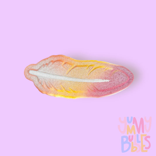 Feather shaped bath bomb painted with orange, yellow, and pink gradient and a white center