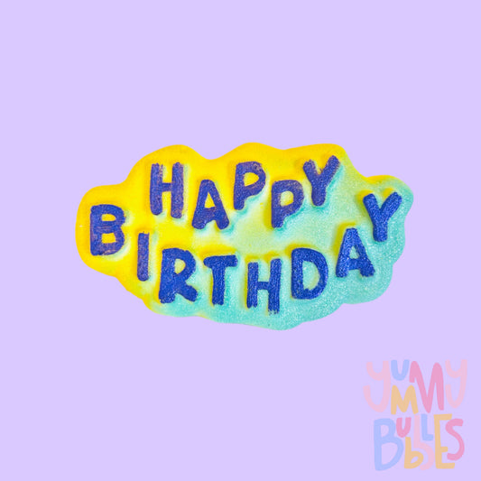 Bath bomb with the text happy birthday painted dark blue on a yellow to light blue gradient