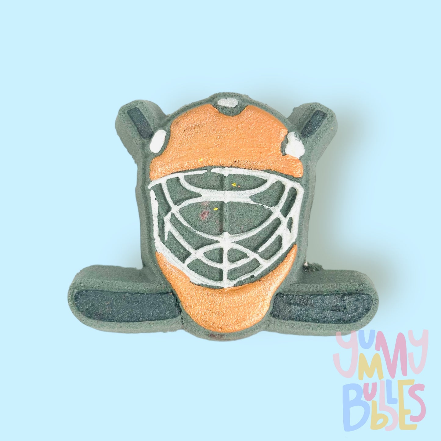 Black hockey helmet shaped bath bomb with hockey sticks in the background. The helmet is painted orange and white and the hockey stick is painted black.