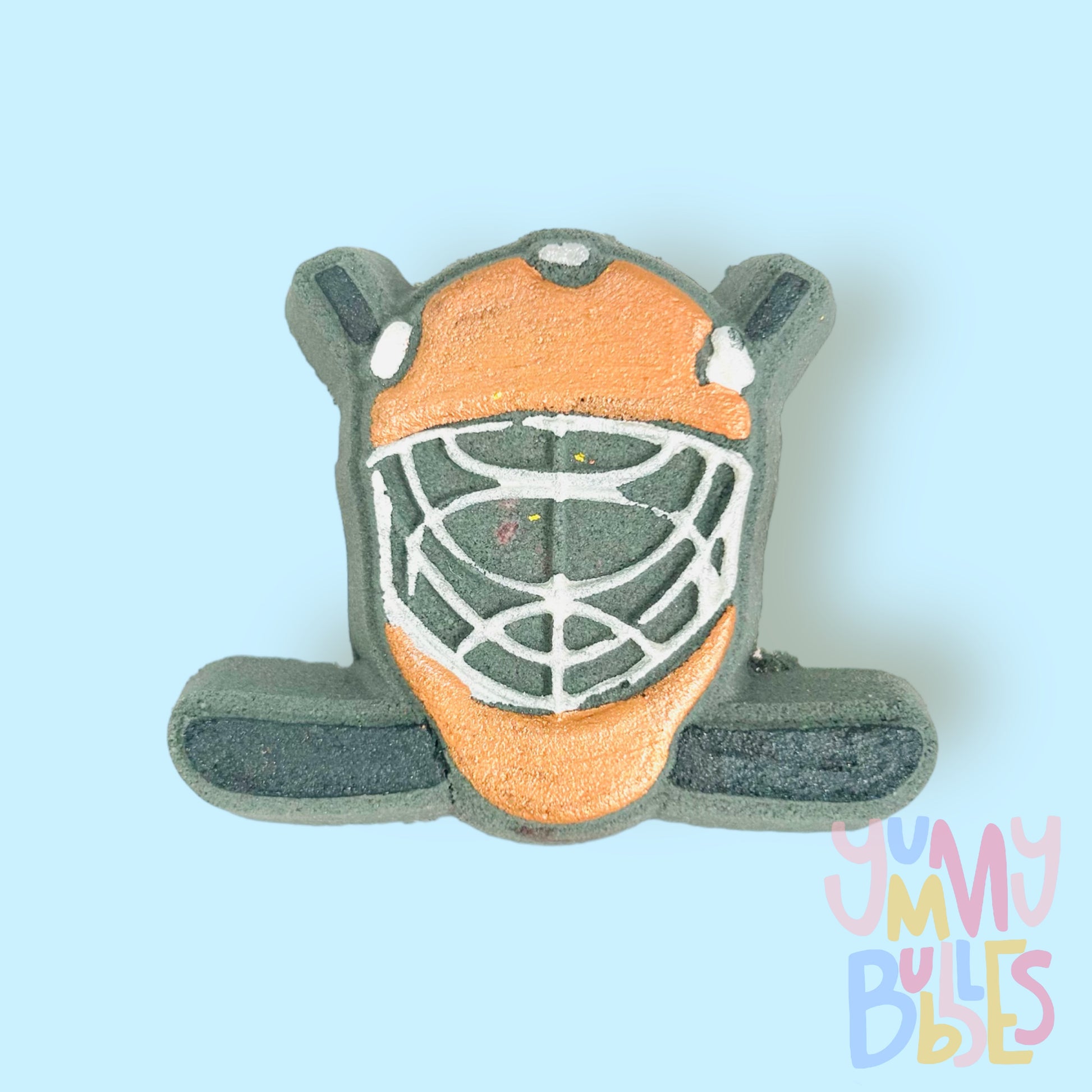 Black hockey helmet shaped bath bomb with hockey sticks in the background. The helmet is painted orange and white and the hockey stick is painted black.