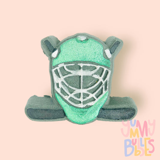Black hockey helmet shaped bath bomb with hockey sticks in the background. The helmet is painted green and white and the hockey stick is painted black.