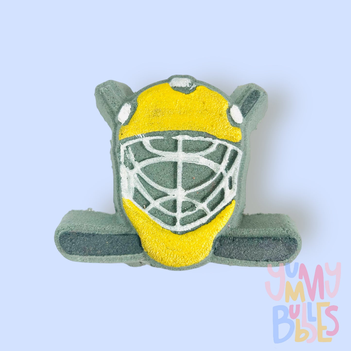 Black hockey helmet shaped bath bomb with hockey sticks in the background. The helmet is painted yellow and white and the hockey stick is painted black.