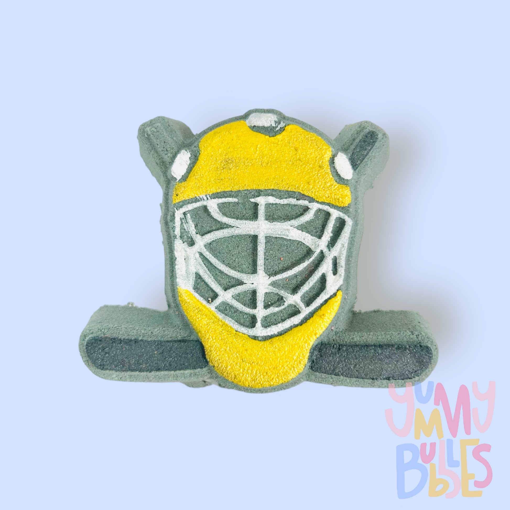 Black hockey helmet shaped bath bomb with hockey sticks in the background. The helmet is painted yellow and white and the hockey stick is painted black.