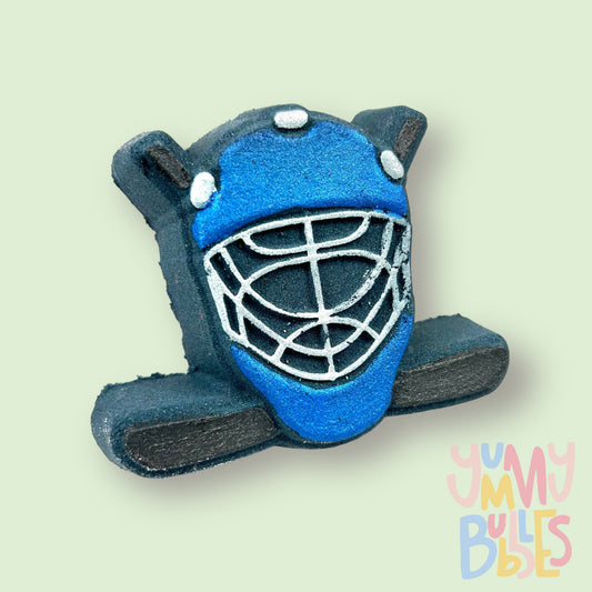 Black hockey helmet shaped bath bomb with hockey sticks in the background. The helmet is painted blue and white and the hockey stick is painted black.