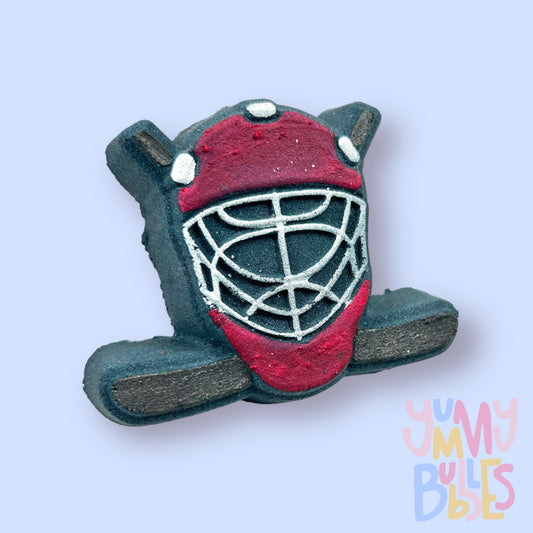 Black hockey helmet shaped bath bomb with hockey sticks in the background. The helmet is painted red and white and the hockey stick is painted black.