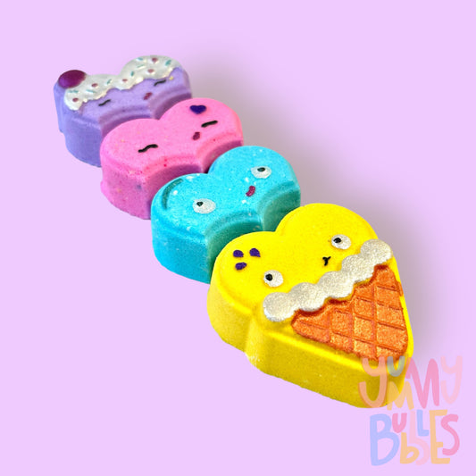 Set of four ice cream shaped bath bombs that are purple, pink, blue, and yellow. Each bath bomb is painted with a variety of colours