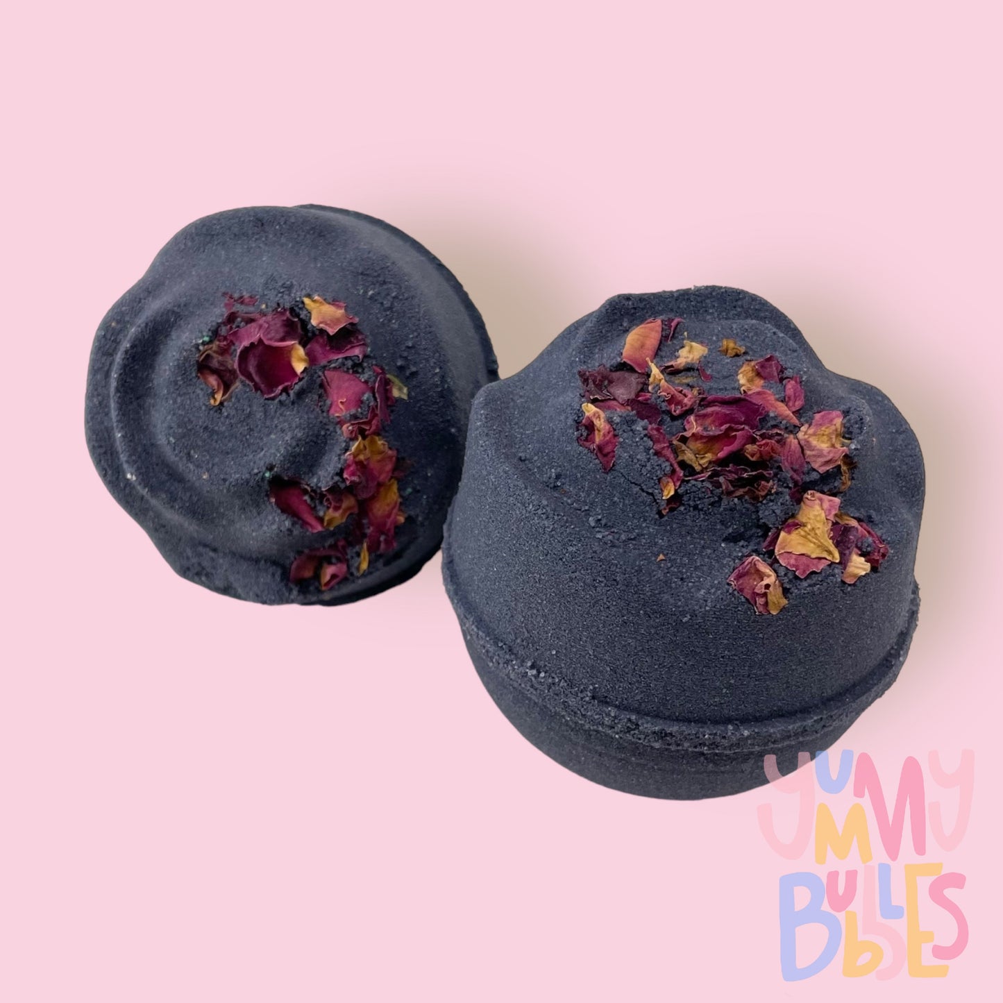Black round shaped bath bomb with rose shaped top and rose petals sprinkled on top