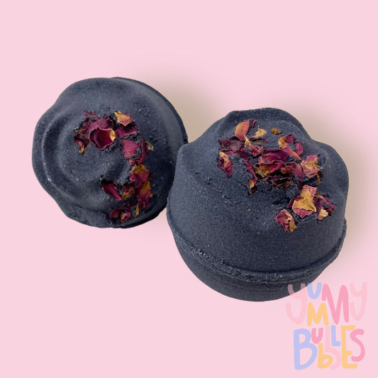 Black round shaped bath bomb with rose shaped top and rose petals sprinkled on top