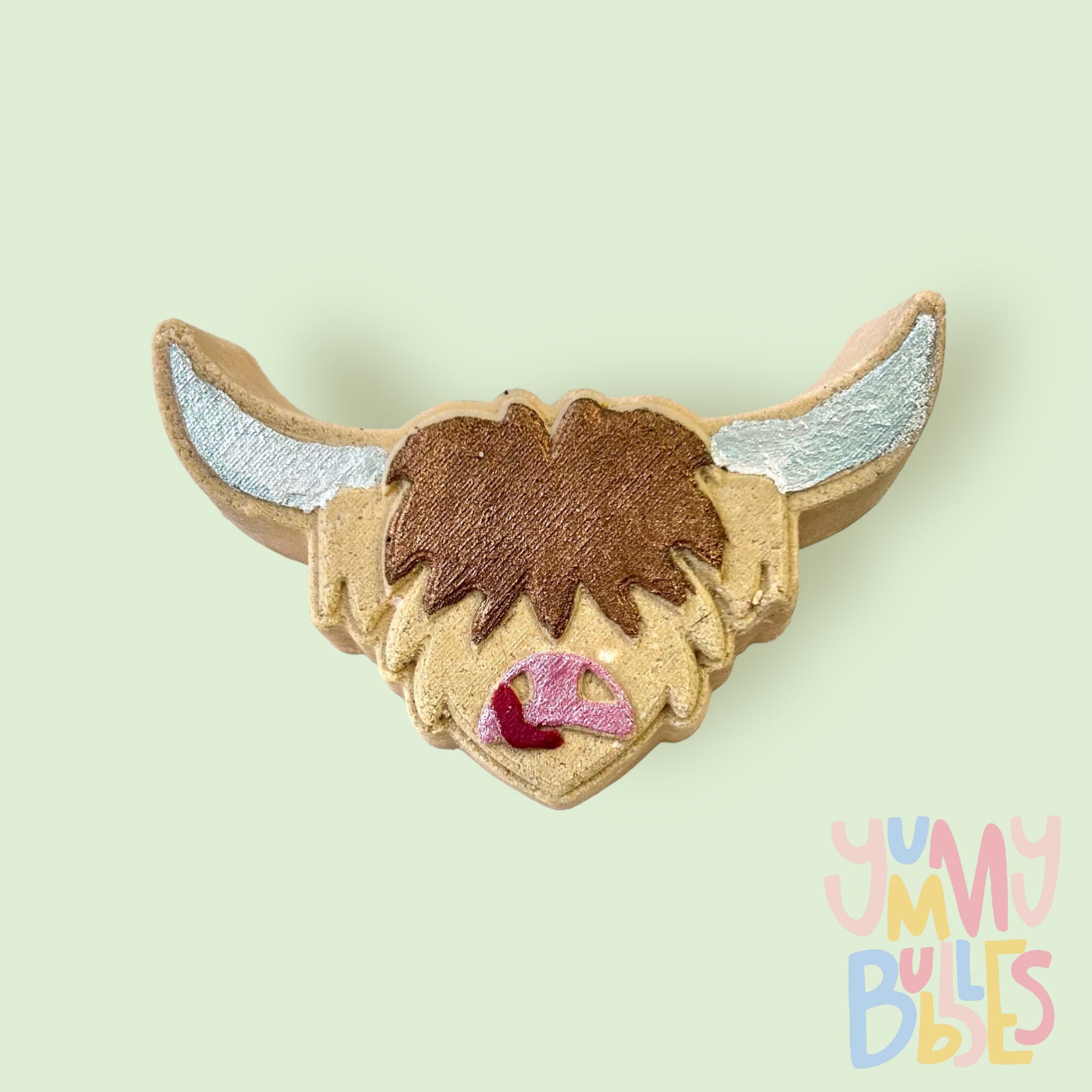 Brown highland cow head shaped bath bomb painted with white, light pink, red, and dark brown