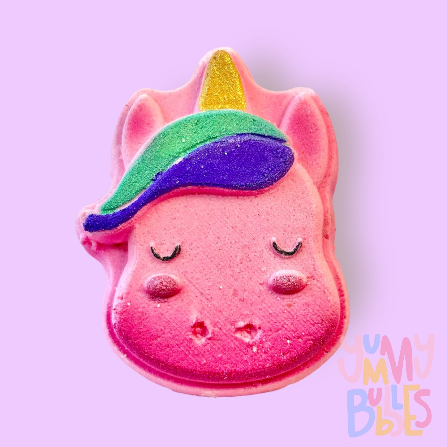 pink unicorn head shaped bath bomb painted with purple, teal, gold, and a dark pink ombre on the bottom