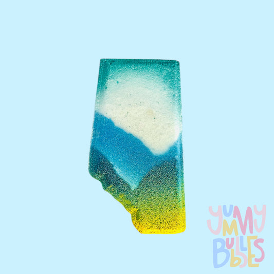 White Alberta shaped bath bomb with blue and dark blue mountains with hints of teal and yellow.